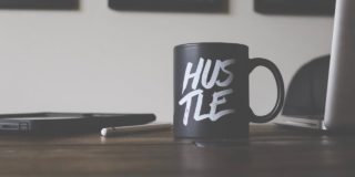 A coffee mug with hustle written on it next to a laptop and pad